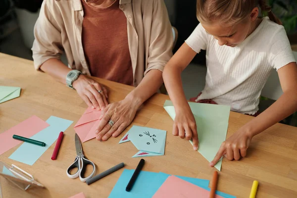 有创意的年轻女孩和她的母亲围坐在桌旁 在家里悠闲自在地做着折纸 一边折叠着彩色的纸 — 图库照片