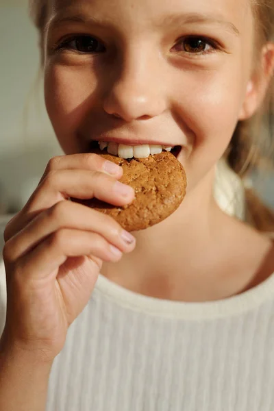 幸せな若いです女の子Biting新鮮なおいしい自家製クッキーの丸型の前に立ってカメラとあなたを見て — ストック写真