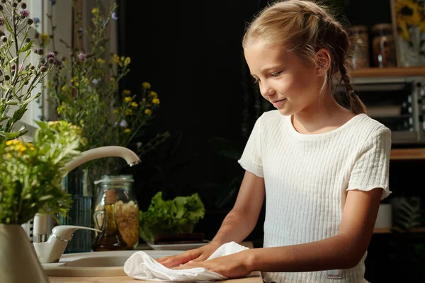 漂亮的少女穿着白色T恤 站在被家用植物环绕的水池旁 用棉签擦拭厨房桌子 — 图库照片