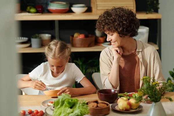 快乐的年轻女人看着她可爱的年轻女儿 一边吃着碗里的意大利面 一边坐在厨房的桌子旁 — 图库照片