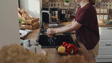 Kafkasyalı genç bir kadının taze sebzeleri durulaması, gündüz vakti mutfakta lavabonun yanında durması.