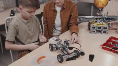 Okulda robotik oyuncak araba modeli üzerinde çalışan iki beyaz gencin aşağı doğru çekimleri.