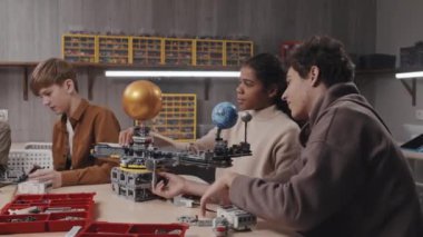 Etnik çeşitlilikte genç bir erkek ve kız, masada oturmuş, robotik dersinde güneş sistemi modeli üzerinde birlikte çalışıyorlar.