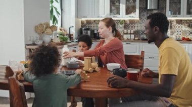 Orta boylu, Afro-Amerikan bir adam, Kafkasyalı bir eş ve evde yemek masasında oturup, kahvaltı yapan ve oyun oynayan iki küçük oğlan.
