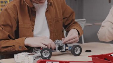 Sınıfta ders sırasında masa başında robot araba modeli yapan tanınmayan bir gencin orta bölümü.