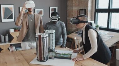 VR gözlüklü üç farklı mimardan oluşan bir ortam, gündüz vakti ofisteki çok katlı apartman düzenine bakıyor.