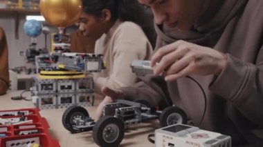 Modern genç kapüşonlu çocuk okuldaki robotik dersinde masa başında araba modelliği yapıyor.