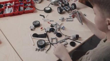 Okuldaki robotik dersinde masa başında oturan beyaz çocuk inşaat malzemeleriyle yeni model binalar açıyor.