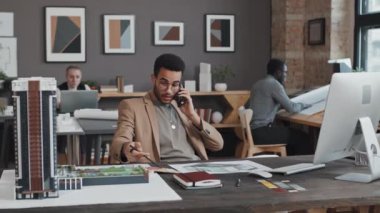 Gündüz vakti masa başında oturan ve cep telefonuyla konuşan genç Mimarın medyumu.