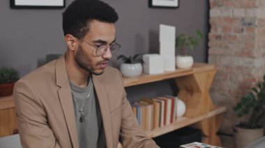 Zeki, çift ırklı mimarın ağır çekimde koltuğunda oturup dizüstü bilgisayar kullanması.