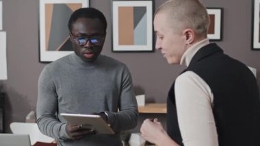 Tablet bilgisayarlı genç Afrikalı Amerikalı bir adam kafatası tıraşlı bir meslektaşla gündüz vakti konuşuyor.