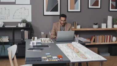 Genç, çift ırklı baş mimarın beli ofiste oturuyor ve taşınabilir bilgisayar kullanıyor.