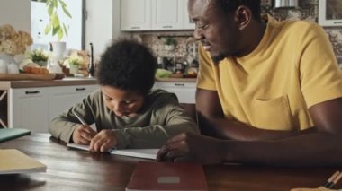 Küçük çocukla ödev yapan, yemek masasında oturup konuşan Afrikalı Amerikalı bir babanın düşük açılı görüntüsü.