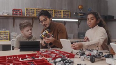 Ortadoğulu genç bir adam, öğrencilerinden birinin robot araba modelini yapmasına yardım ediyor.