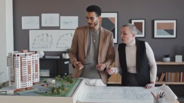 Modern ofiste masa başında oturan ve apartman planlarıyla çalışan iki ırklı ve kadın mimari tasarımcılardan oluşan genç bir ortam.