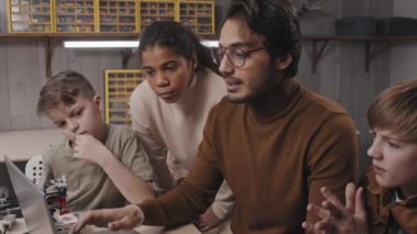 Genç ve yakışıklı Orta Doğu öğretmeninden uzaklaşın. Dizüstü bilgisayarın önünde oturmuş, öğrencisine robotik dersini açıklarken.