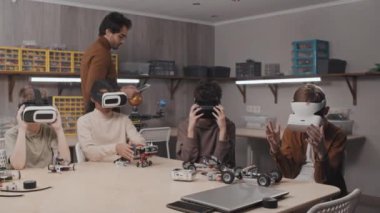 Modern ortaokulda robotik dersinde VR kulaklık kullanan bir grup çocuk. Genç öğretmen onlarla çalışıyor.