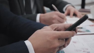 Kesilmiş işadamının yan görüntüsü, masada oturuyor, akıllı telefon kullanıyor.