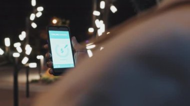 Tanımlanamayan siyahi bir adamın gece vakti dışarıda dikilip akıllı telefon ekranına bakarak online banka işleminin bitmesini beklemesi.