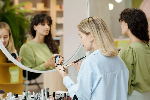 年轻顾客站在化妆品超级市场的镜子前 用刷子和紧凑型粉末检测美容产品 — 图库照片