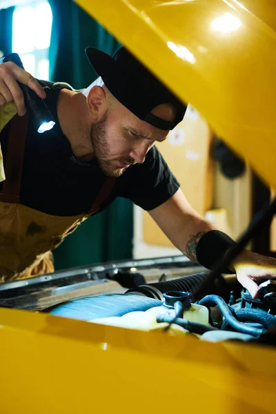 Poważny Mechanik Samochodowy Latarką Pochylającą Się Nad Otwartą Maską Żółtego — Zdjęcie stockowe