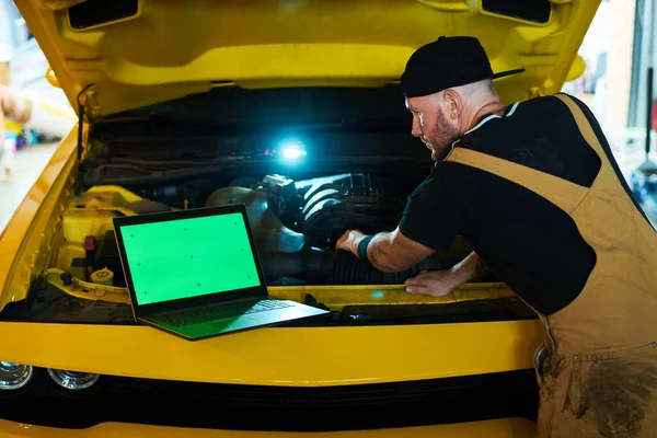 Młody Mechanik Trzymając Rękę Silniku Samochodowym Patrząc Zielony Ekran Laptopa — Zdjęcie stockowe