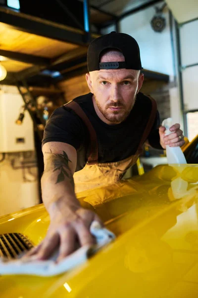 从事维修工作的年轻男工 修理工作后 用一瓶洗涤剂清洗黄色汽车的车盖 — 图库照片