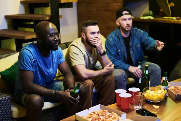 三个不同文化的男人坐在桌旁 一边喝着薯片啤酒 一边在车库里观看足球比赛的转播 — 图库照片