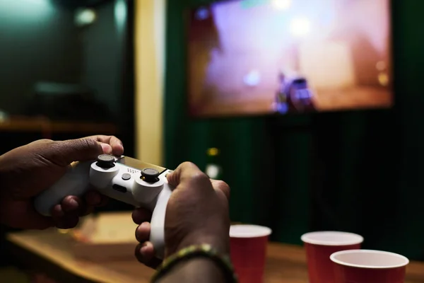 若いアフリカ系アメリカ人の男性の手ビデオゲーム中に設定されたテレビの画面上のデバイスを指示しながら コントローラ上のボタンを押す — ストック写真