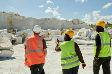 Beyaz kayalara doğru ilerleyen ve onun özelliklerini tartışan mermer ocaklarının kültürler arası birkaç genç işçisinin arka görüntüsü.