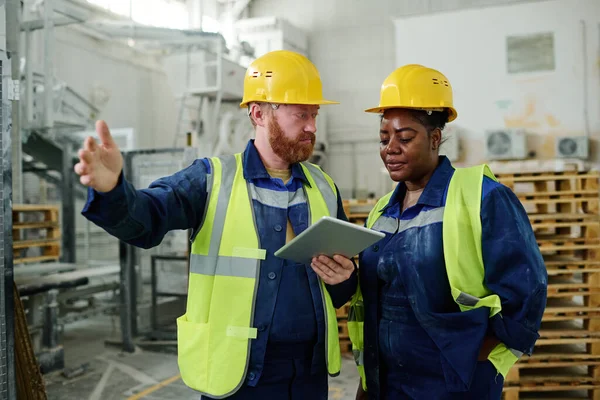 年轻自信的男性工程师 穿着工作服 戴着安全帽 在会上解释新项目的女性同事的技术时刻 — 图库照片