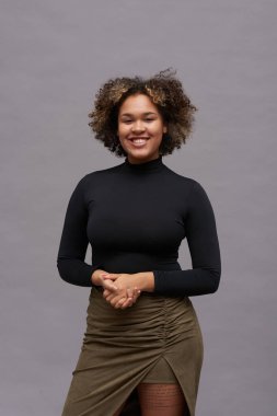 Genç, neşeli, gündelik giysili manken kız izolasyonda sana bakarken ellerini önünde tutuyor.