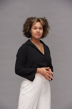 Fotoğraf çekimi sırasında kameranın önünde gri arkaplan karşısında şık giyinen çok ırklı genç bir kadın.