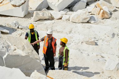 Bir grup kültürler arası taş ocağı işçisi, fabrika bölgesinde onlardan birinin önünde dururken mermer kayaların kalitesini kontrol ediyorlar.