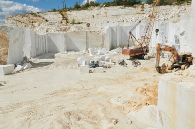 Kalın beyaz kaya duvarları ve bölgede çalışan iki inşaat makinesiyle çevrili geniş mermer ocağının bir parçası.
