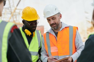 Genç, kendinden emin ustabaşı belgeye çalışma planıyla işaret ederken aynı zamanda Afrika kökenli Amerikalı erkek astına da açıklamasını yapıyor.