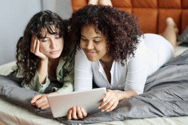 Evdeki mutlu genç lezbiyen çift film seyrediyor ya da çift kişilik rahat bir yatakta dinlenirken internetten mal seçiyor.