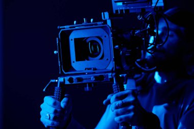 Genç kameraman veya fotoğrafçının elleri karanlıkta reklam çekerken tripodun sapıyla sabitlenmiş.