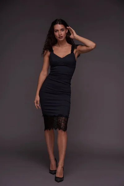 若いです美しいですブルネット女性でシルク黒ドレスに立ってカメラの前に灰色の背景に対して写真セッション中にスタジオ — ストック写真