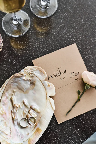 2つのリング 招待状 新鮮な白のバラとテーブルの上にシャンパンとフルートとパールシェルの結婚式の組成のフラットレイ — ストック写真