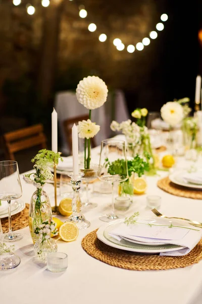 皿の2列の間に立つキャンドルや白いダリアの花で飾られた結婚式のパーティーのために用意されたテーブルの一部 — ストック写真