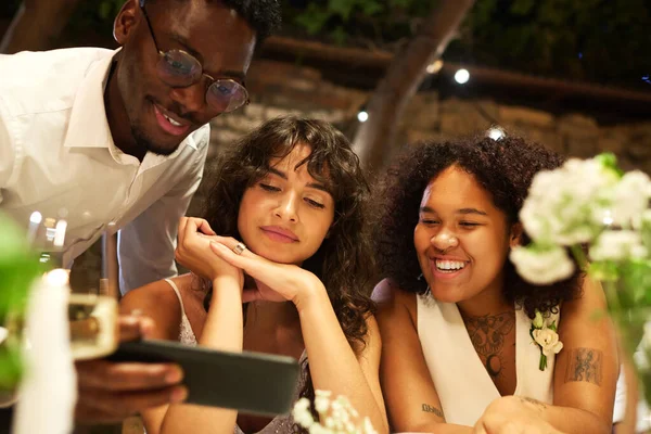 两个快乐的年轻女同性恋新娘和黑人在婚宴上坐在喜庆桌旁进行视频交流 — 图库照片