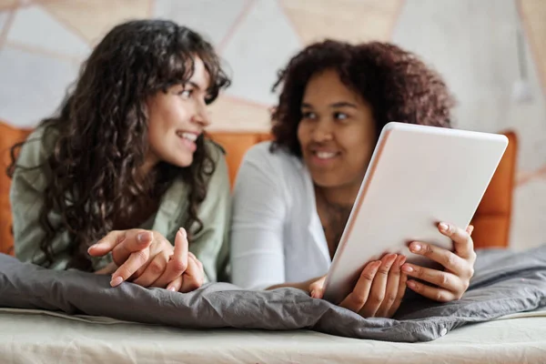 年轻的非洲裔美国女人手握数码平板电脑 一边和女朋友聊天 一边在舒适的双人床上放松自己 — 图库照片