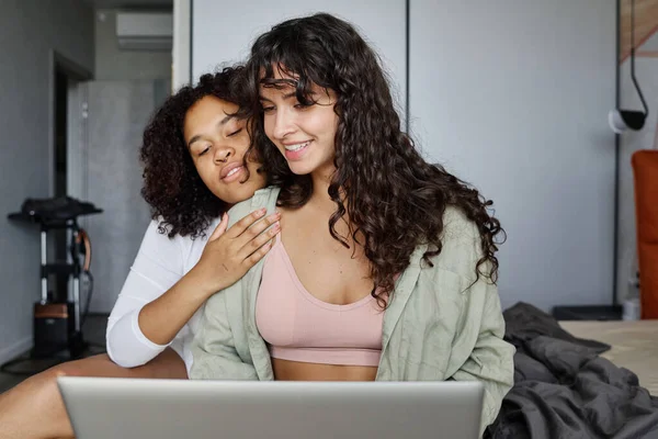 年轻多情的非洲裔美国女人抱着她的女朋友 坐在笔记本电脑前和网络前的双人床上 — 图库照片