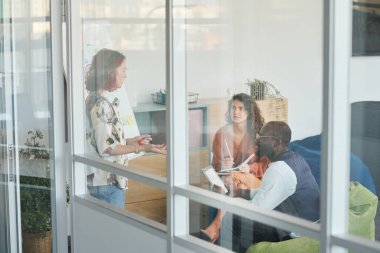 Seminerde sunum noktalarını tartışan bir grup kültürler arası genç iş arkadaşı ya da büyük pencerenin arkasındaki ofiste çalışma toplantısı