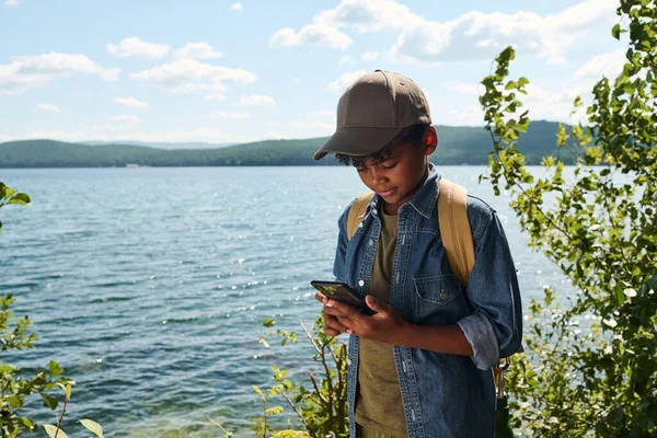 Młodzieńczy Backpacker Casualwear Pomocą Smartfona Podczas Stania Nad Jeziorem Lub — Zdjęcie stockowe
