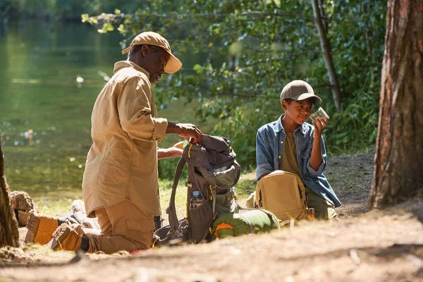 Wiek Afroamerykanin Rozpakowuje Plecak Stojąc Kolanach Ścieżce Przed Wnukiem Słoikiem — Zdjęcie stockowe