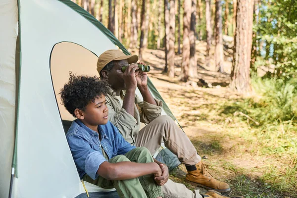 双眼鏡を持つ熟女黒男で彼の目に座っているテントの横に彼の孫にカジュアルながら 両方のハイキング旅行中に休息を持っている — ストック写真