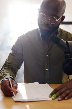 Genç, kel, siyah bir adam, mikrofonun önünde stüdyoda otururken misafirle röportaj yapmak için hazırlandı.