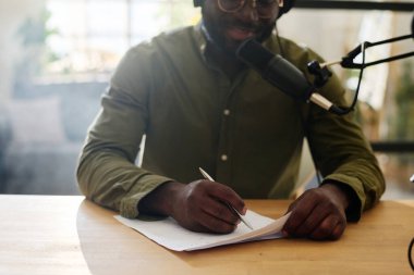 Genç siyahi bir adamın, mikrofonla konuşurken sorulacak sorularla kağıda işaret ettiği yakın plan.
